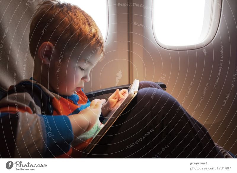 Kleines Kind mit Tablet-Computer auf dem Schoß sitzen durch den Beleuchter im Flugzeug Freude Freizeit & Hobby Spielen Ferien & Urlaub & Reisen Ausflug