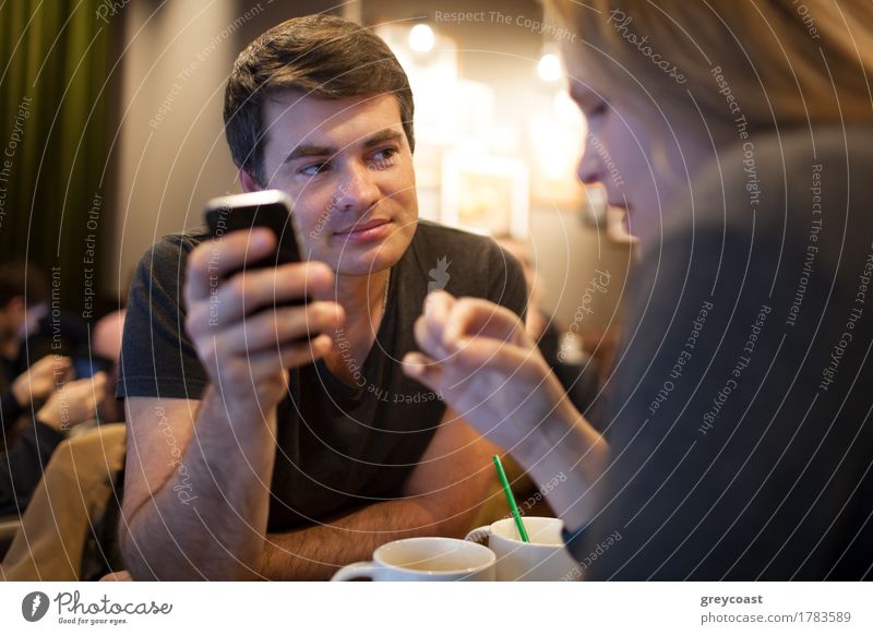 Junger Mann mit Handy während der Sitzung mit einem Mädchen in einem Café, aber sein Blick wird von jemand anderem angezogen Tee Telefon PDA Mensch Junge Frau