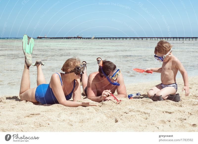 Mutter, Vater und kleiner Sohn im Sommerurlaub am Meer, Sie tragen Schnorchel und Flossen beim Liegen und Spielen am Strand Freude Ferien & Urlaub & Reisen Kind