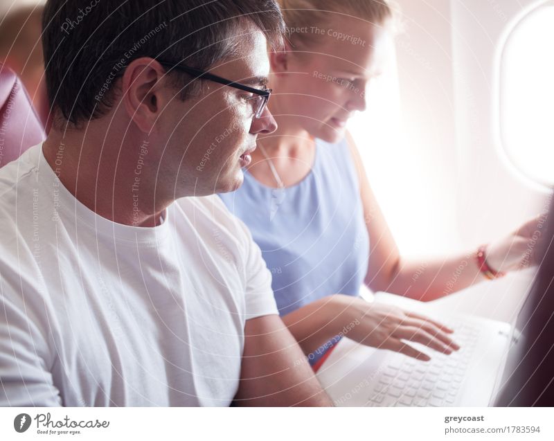 Mann und Frau sitzen daneben und schauen sich während des Fluges etwas im Laptop an. Ferien & Urlaub & Reisen Ausflug Business Computer Notebook