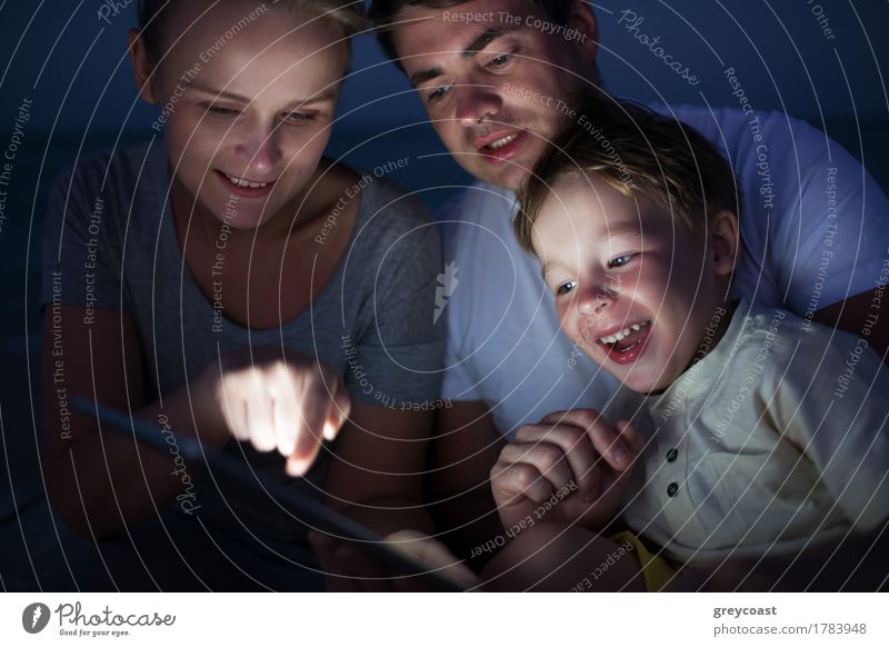 Glückliche dreiköpfige Familie mit Pad spät am Abend. Lachendes Kind schaut auf den Bildschirm, wo die Mutter auf etwas zeigt Freude Freizeit & Hobby Spielen