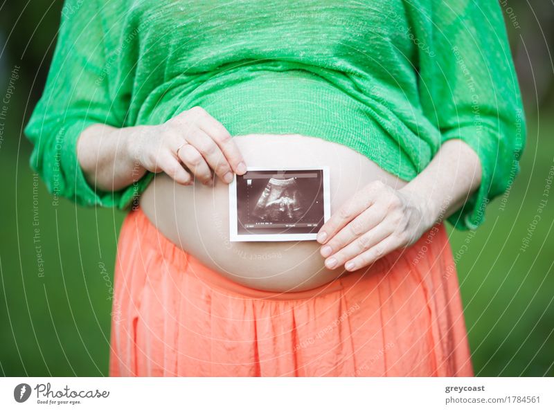 Nahaufnahme einer schwangeren Frau, die einen Ultraschallscan vor ihrem nackten Bauch hält. Das Glück der Schwangerschaft Medikament Sommer Erwachsene Mutter