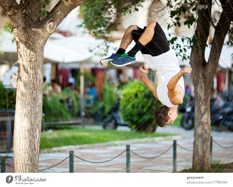Junge Extremsportler tun Frontflip zwischen den Bäumen. Stadt Straße mit Outdoor-Café im Hintergrund Lifestyle Freiheit Sommer Sport Mensch Mann Erwachsene Baum