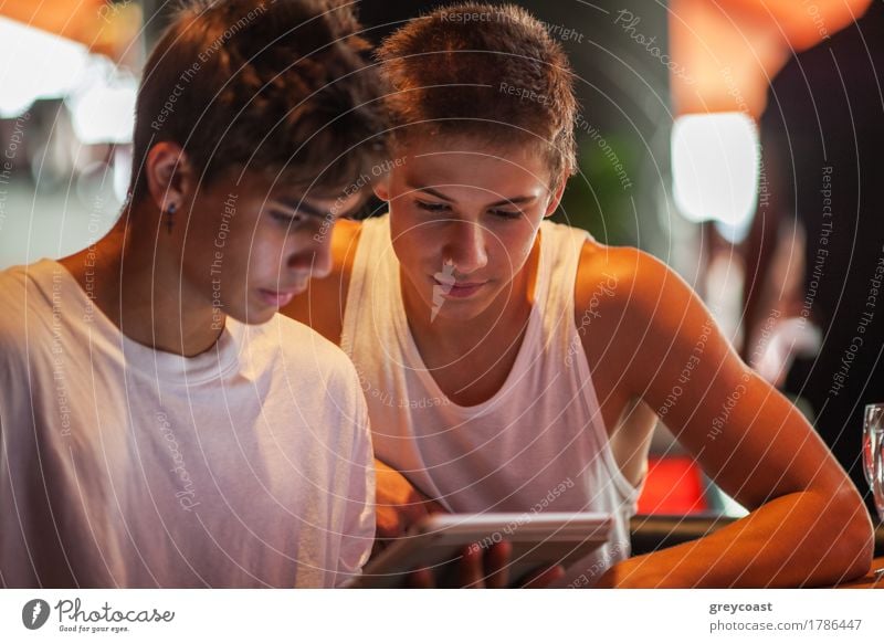 Zwei Teenager in weißen Sport-Shirts mit Tablet-PC in der Cafeteria. Sie schauen auf den Pad-Bildschirm Freizeit & Hobby Entertainment Computer Internet Mensch