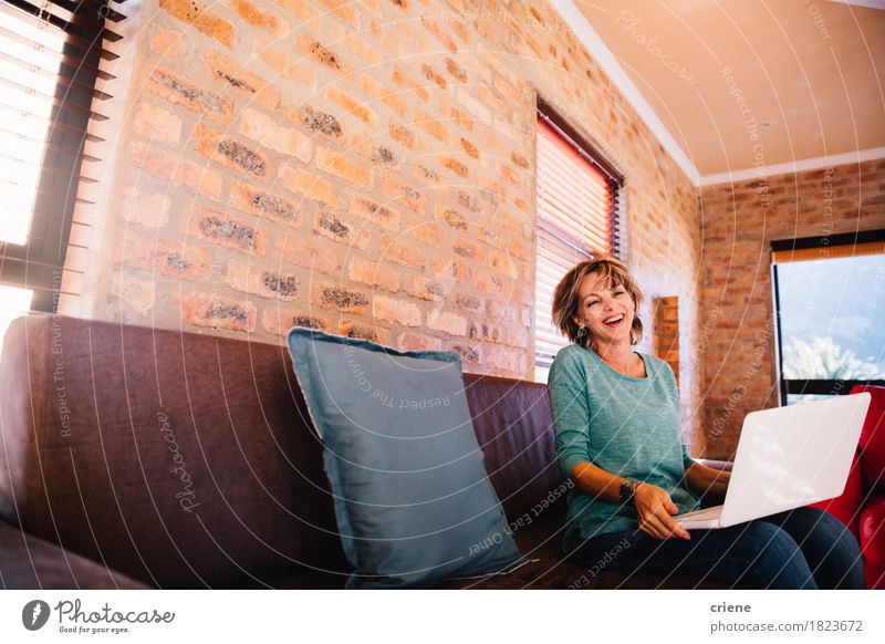 Frau, die den Spaß zu Hause hat, der mit ihrem Laptop auf Couch lacht Lifestyle Freude Arbeit & Erwerbstätigkeit Arbeitsplatz Business Computer Notebook