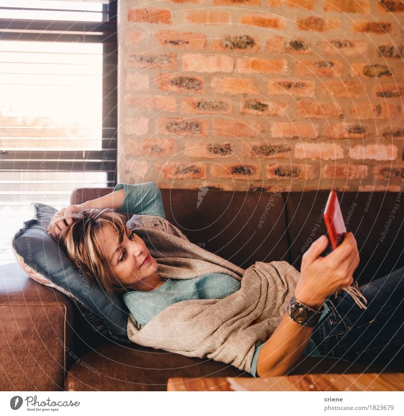 Fällige Frau simst Nachricht mit Smartphone lesen Wohnzimmer Telefon Handy PDA Technik & Technologie Internet Mensch Erwachsene Senior modern bequem reif Texten