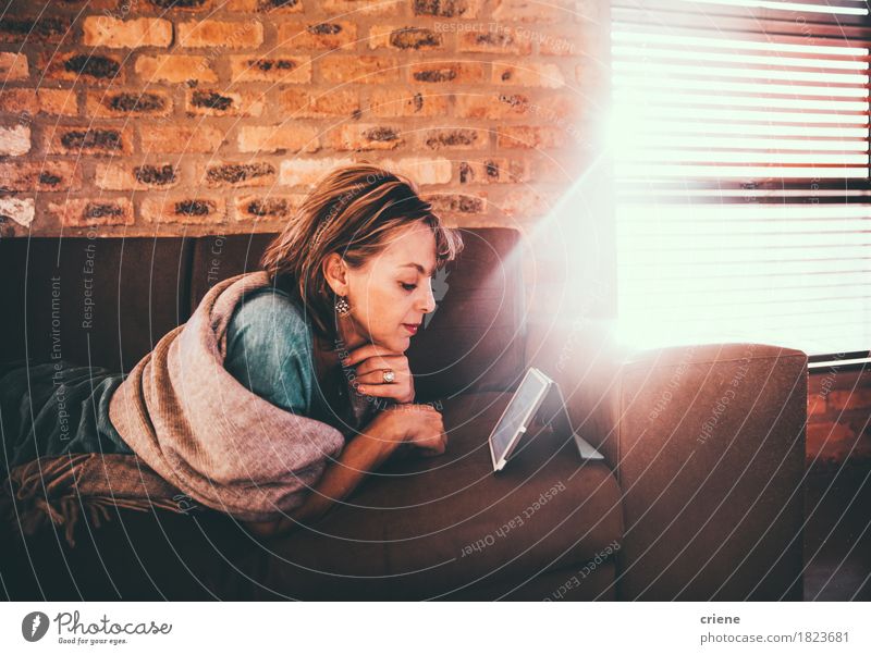 Reife kaukasische Frauenlesezeitung auf ihrer digitalen Tablette Lifestyle Erholung Freizeit & Hobby lesen Sofa Wohnzimmer Arbeit & Erwerbstätigkeit Business