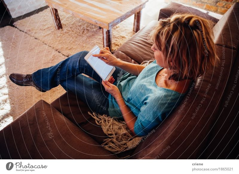 reife Frau, die auf Sofa unter Verwendung der digitalen Tablette sitzt Lifestyle lesen Haus Wohnzimmer Büro Business Computer Technik & Technologie