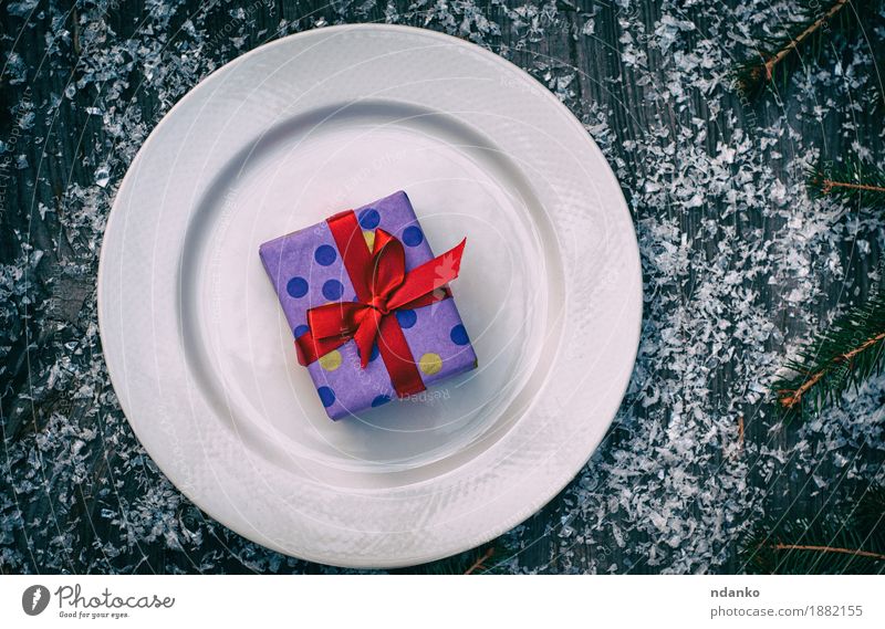Verpacktes Geschenk mit einem roten Band auf einer weißen Platte Frühstück Mittagessen Abendessen Geschirr Teller Besteck Schnee Dekoration & Verzierung Tisch