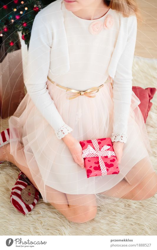 Tragendes Kleid des Mädchens, welches das Weihnachtsgeschenk sitzt auf einem Teppich hält Lifestyle Dekoration & Verzierung Feste & Feiern Weihnachten & Advent