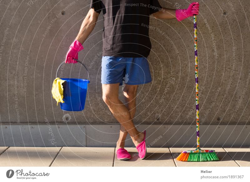 Ein Hausmann in rosaroten Hausschuhen und Putzutensilien Sommer maskulin Mann Erwachsene Körper 1 Mensch 30-45 Jahre Mauer Wand Besen Eimer Handschuhe Putztuch