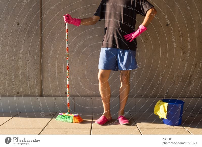 Ein Hausmann in rosaroten Hausschuhen und Putzutensilien Sommer maskulin Mann Erwachsene Partner Körper 1 Mensch 30-45 Jahre Mauer Wand T-Shirt Besen Besenstiel
