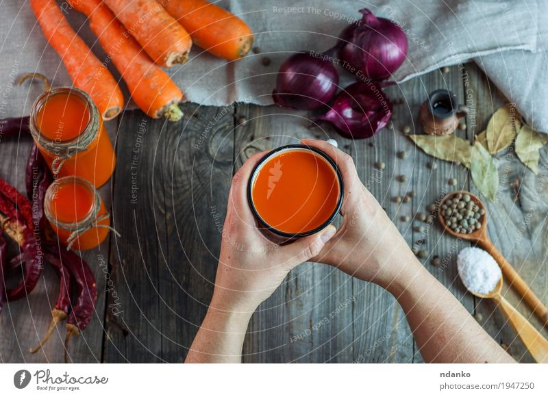 weibliche Hände, die einen Eisenbecher mit Karottensaft halten Lebensmittel Gemüse Kräuter & Gewürze trinken Saft Tasse Becher Löffel Körper Tisch Junge Frau
