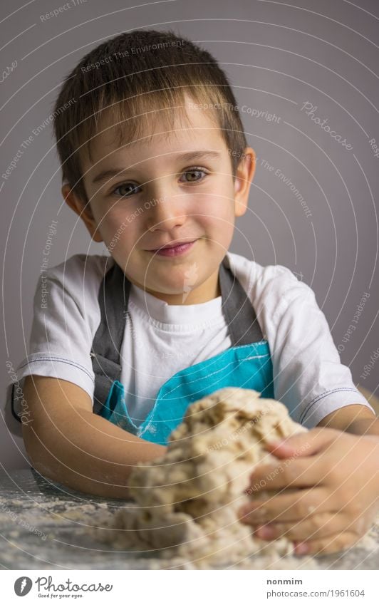 Kleiner Junge knetet rohen Pizzateig und -c $ lächeln Teigwaren Backwaren Brot Freude Küche Kind Kindheit Lächeln machen blau unschuldig reizvoll Schürze backen
