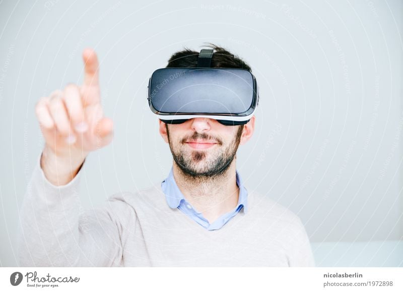 Mittlerer erwachsener Mann, der Virtual-Reality-Simulator Brille trägt, mit dem Finger zeigt und weißer Hintergrund virtuelle Realität VR-Brille