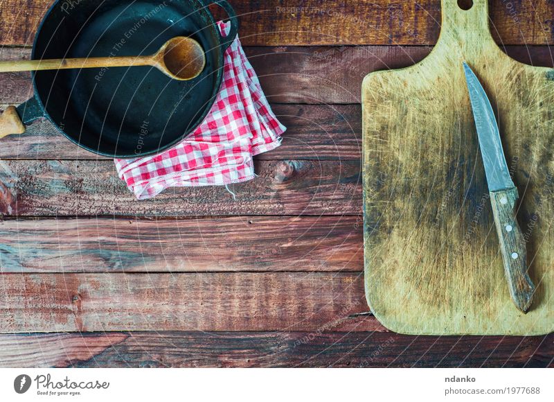 schwarze Gusseisenwanne und Schneidebrett auf brauner Holzoberfläche Geschirr Pfanne Messer Löffel Tisch Küche Restaurant Werkzeug Stoff Metall Stahl alt oben