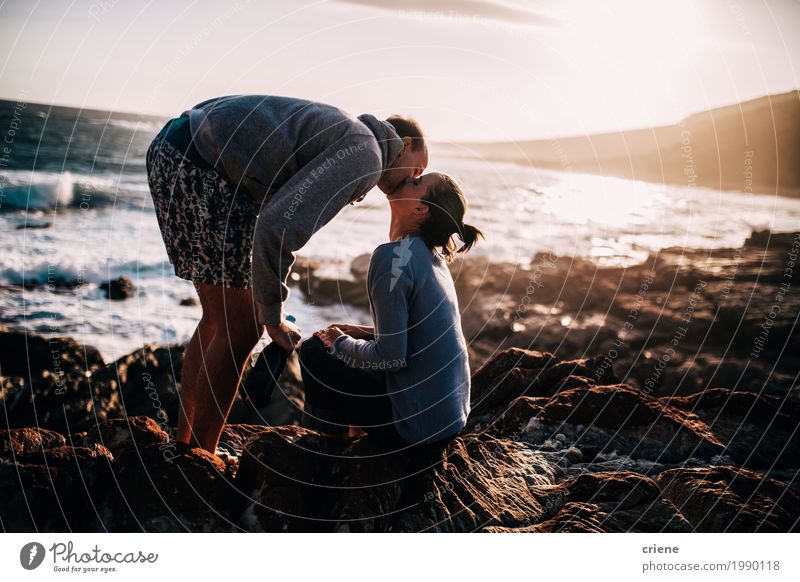 Glückliche junge erwachsene Paare, die am Strand auf Felsen küssen Lifestyle Freude Sommerurlaub Meer Junge Frau Jugendliche Junger Mann Partner Küssen Lächeln