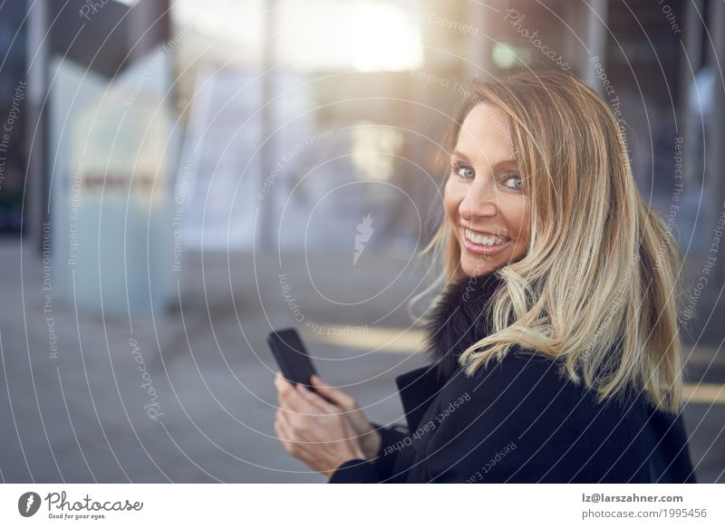Lächelnde attraktive Frau, die über ihrer Schulter schaut Glück Gesicht Business Telefon PDA Erwachsene 1 Mensch 30-45 Jahre Stadt Straße blond Freundlichkeit