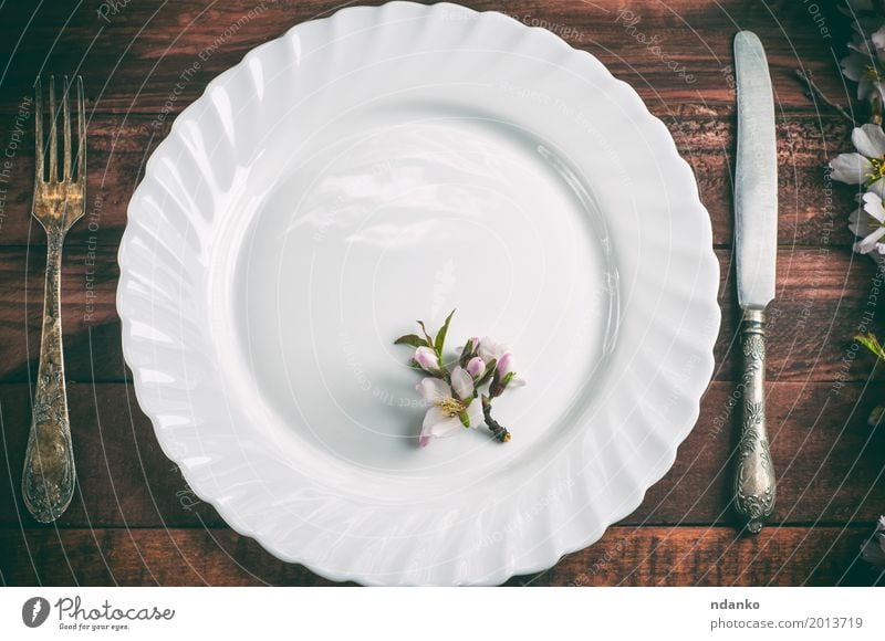 Platte mit einer Gabel und Messer auf einer braunen Holzoberfläche Mittagessen Abendessen Teller Besteck Tisch Küche Restaurant Blume Metall alt oben retro weiß