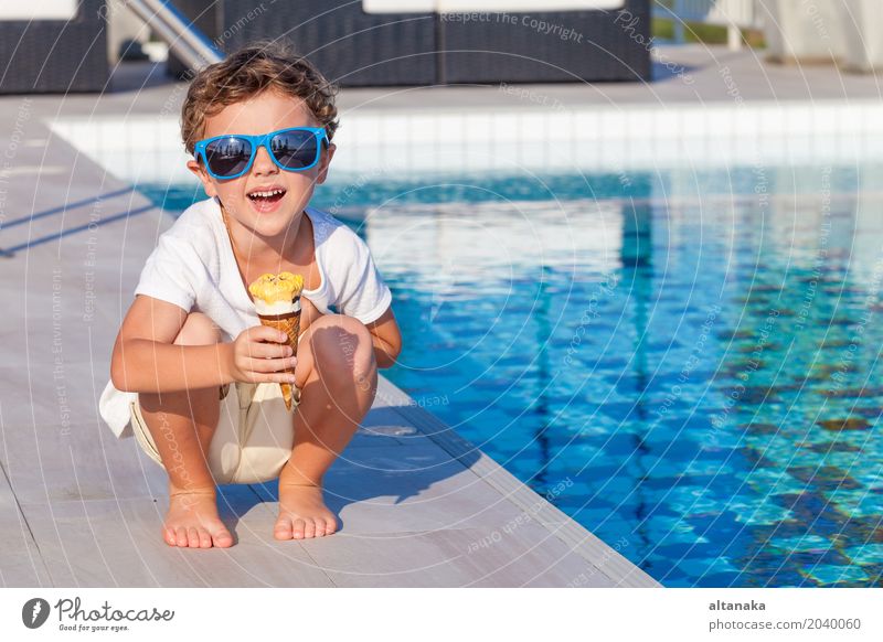 Glücklicher kleiner Junge mit der Eiscreme, die nahe einem Swimmingpool sitzt Dessert Essen Lifestyle Freude schön Erholung Freizeit & Hobby Spielen