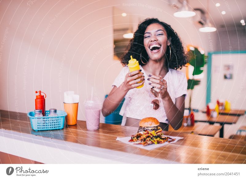Junge glückliche Frau, die Hamburger und Fischrogen im Restaurant genießt Brötchen Essen Mittagessen Fastfood Lifestyle Freude Sommer Junge Frau Jugendliche