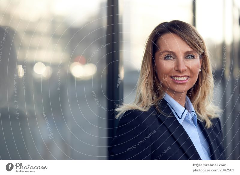 Überzeugter weiblicher Manager, der auf Fenster sich lehnt Glück Gesicht Business Frau Erwachsene 1 Mensch 30-45 Jahre Anzug blond Lächeln stehen modern blau