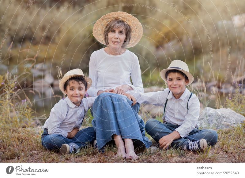 Großmutter mit ihren Enkelkindern, die auf dem Gebiet sitzen Lifestyle Mensch maskulin feminin Kind Kleinkind Junge Weiblicher Senior Frau Geschwister Bruder