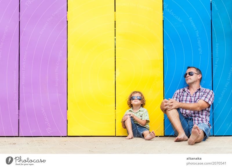 Vater und Sohn entspannen in der Nähe des Hauses in der Tageszeit. Sie sitzen in der Nähe sind die bunten Wand. Konzept der freundlichen Familie. Lifestyle