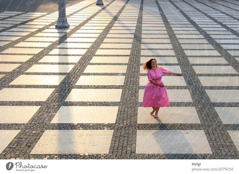 Frau mit langen brünetten wehenden Haaren und rosa Kleid tanzt barfuß auf einem großen gepflasterten Platz im Gegenlicht Mensch feminin Erwachsene 1 45-60 Jahre