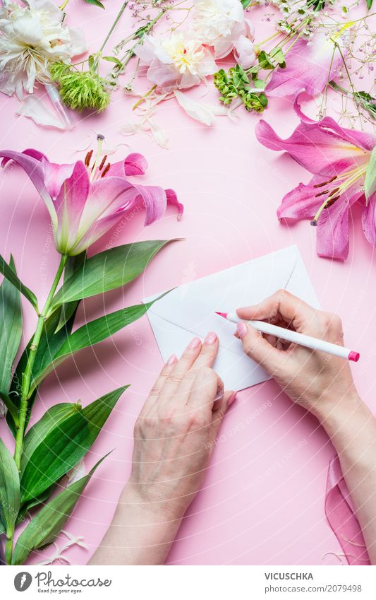 Weibliche Hände schreiben Grußkarte auf rosa Tisch mit Blumen Lifestyle Stil Design Häusliches Leben Dekoration & Verzierung Feste & Feiern Valentinstag