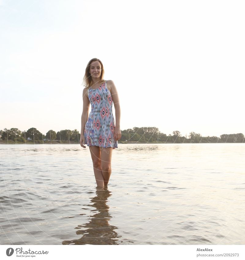 Gegenlichtportrait einer jungen Frau im Sommerkleid die mit den Füßen im Wasser steht Lifestyle Freude schön Körper Wohlgefühl Ausflug Junge Frau Jugendliche