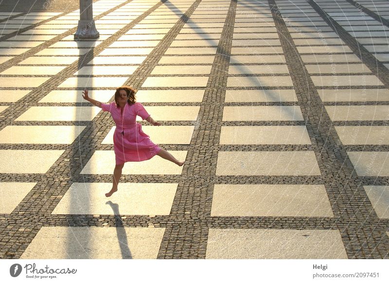 Frau mit langen brünetten Haaren und rosa Kleid hüpft barfuß auf einem großen gepflasterten Platz im Gegenlicht Mensch feminin Erwachsene 1 45-60 Jahre Chemnitz