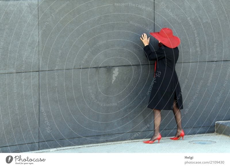 Rückansicht einer elegant gekleideten Dame mit schwarzem Mantel, rotem Hut und roten Pumps vor grauer Wand Mensch feminin Frau Erwachsene Weiblicher Senior 1