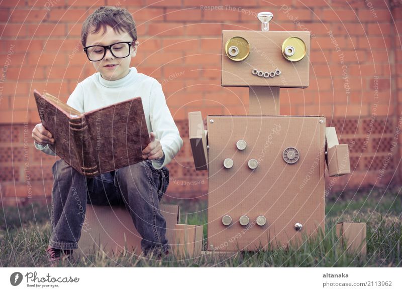 Ein kleiner Junge liest im Freien einem Roboter aus Pappkartons vor. Konzept von Wissenschaft und Bildung. Lifestyle Freude Glück schön Erholung