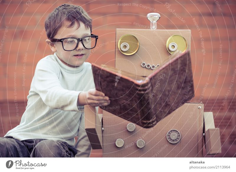 Ein kleiner Junge liest im Freien einem Roboter aus Pappkartons vor. Konzept von Wissenschaft und Bildung. Lifestyle Freude Glück schön Erholung