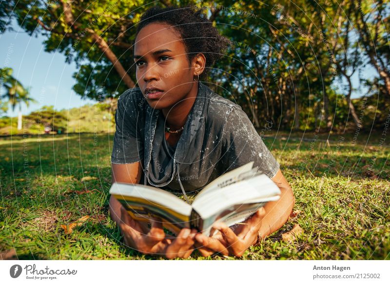 Junge afroamerikanische Frau beim Lesen eines Buches, das auf dem grünen Rasen liegt. Lifestyle feminin Junge Frau Jugendliche 1 Mensch 18-30 Jahre Erwachsene