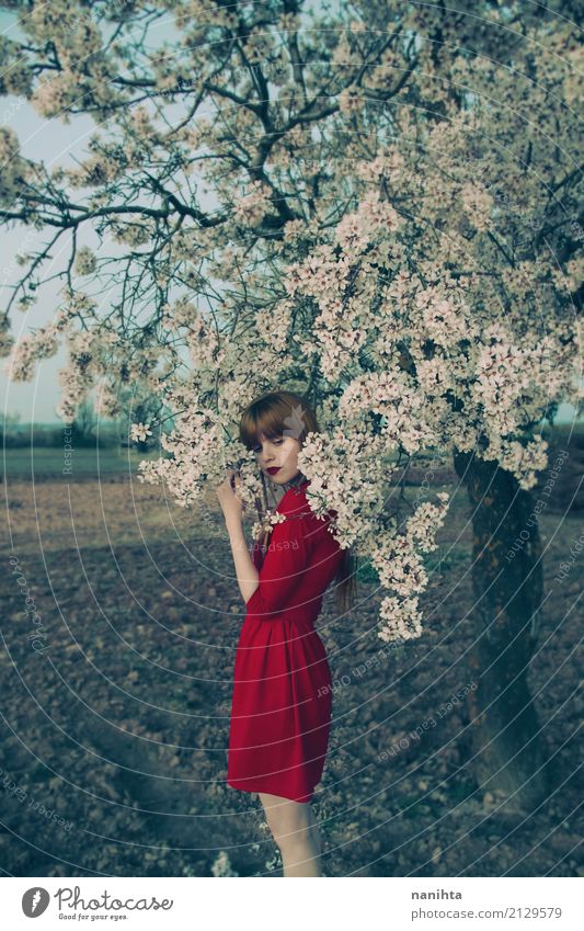 Junge Frau mit dem roten Kleid, das nahe einem blühenden Baum aufwirft elegant Stil harmonisch Sinnesorgane Erholung ruhig Duft Mensch feminin Jugendliche 1