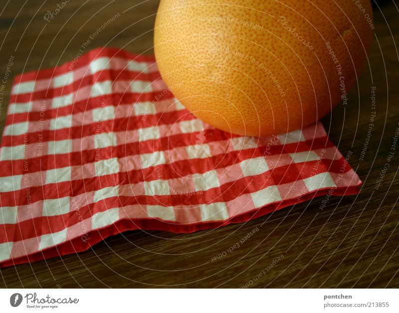 Eine Grapefruit auf einer rot-weiß karierten Serviette auf einem Holztisch. Farben und Firmen. Rund und eckig Lebensmittel Frucht Ernährung Häusliches Leben
