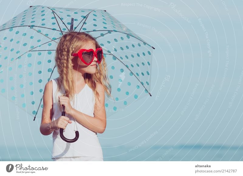 Kleines Mädchen mit dem Regenschirm, der auf dem Strand zur Tageszeit steht Lifestyle Freude Glück schön Erholung Freizeit & Hobby Spielen