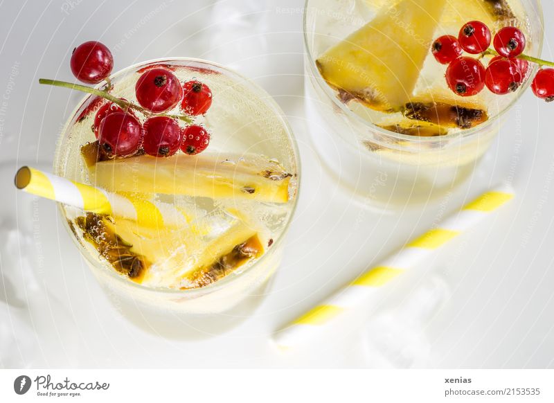 Erfrischendes Getränk mit Ananas, Johannisbeeren, gelben Trinkhalmen und Eiswürfel auf weißem Grund Erfrischungsgetränk Trinkwasser Frucht Limonade Glas