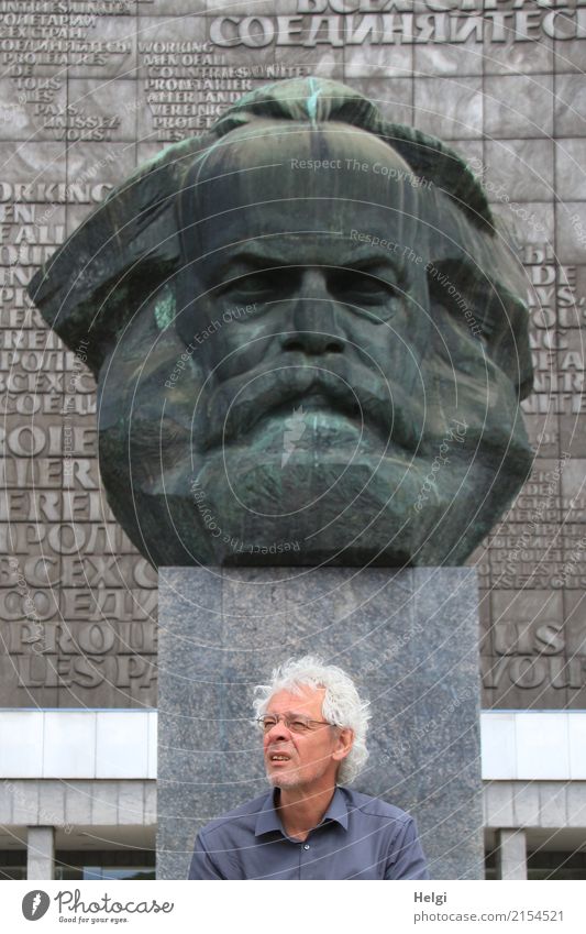 männlicher Senior mit silbergrauen Locken, Brille und Dreitagebart sitzt vor dem Karl-Marx-Denkmal in Chemitz Mensch maskulin Männlicher Senior Mann 1