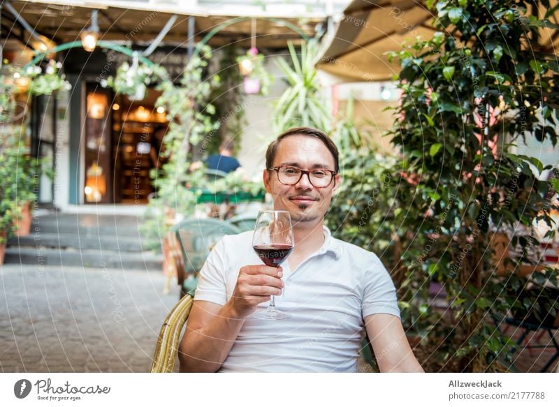 Mann mit Weinglas sitzt im Stuhl und ist zufrieden 1 Mensch Junger Mann sitzen Tag Außenaufnahme Wärme Sommer Rotwein Alkohol trinken Zuprosten Restaurant