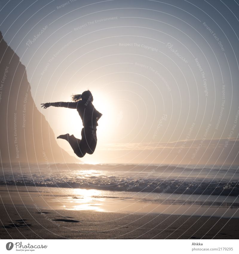 Junger Mensch springt genau vor der Sonne am Strand an den Bergen im Gegenlicht sportlich Fitness Leben Zufriedenheit Sinnesorgane Ferien & Urlaub & Reisen