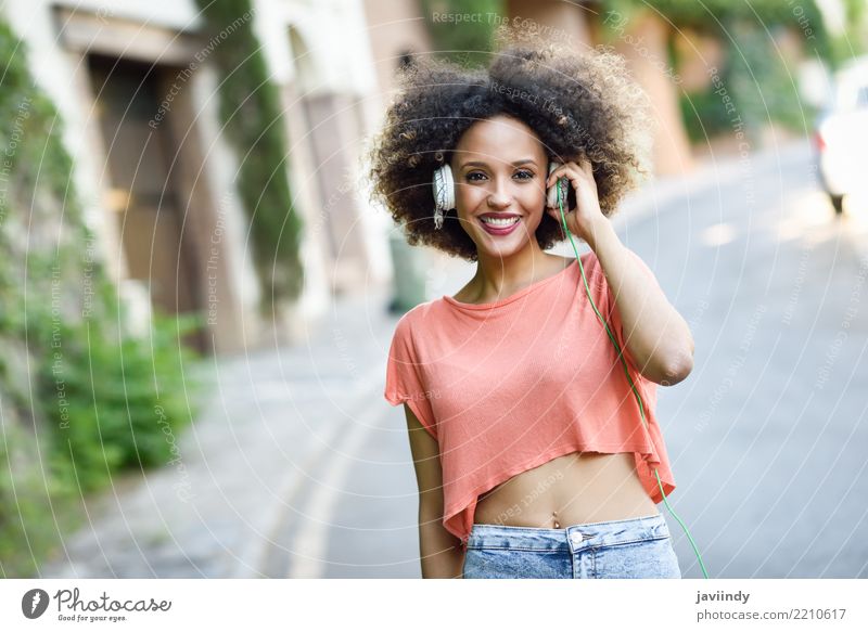 Porträt eines jungen, attraktiven schwarzen Mädchens im städtischen Hintergrund, das der Musik mit Kopfhörern lauscht. Lifestyle Freude Glück schön
