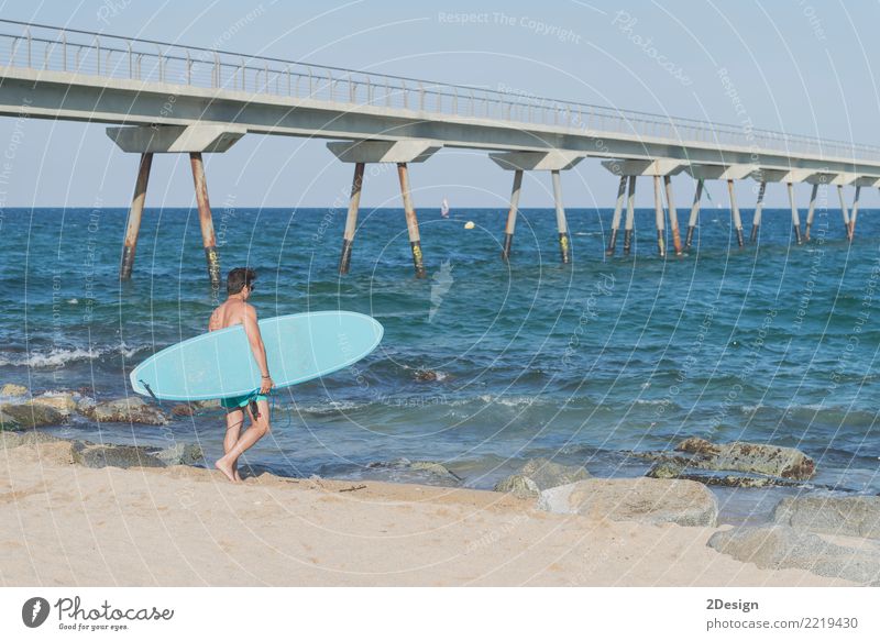 Junger attraktiver Surfer, der sein Surfbrett am Strand hält Lifestyle Freude Ferien & Urlaub & Reisen Sommer Sonne Meer Wellen Sport Mann Erwachsene