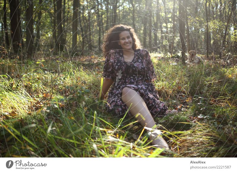 Portrait einer großen, schönen Frau mit langen, dunklen, lockigen Haaren im Wald - im Hintergrund wartet ein blonder Labrador Leben Sinnesorgane Junge Frau