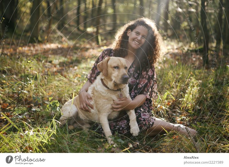 Portrait eines jungen, blonden Labradors mit einer jungen, großen, schönen Frau mit langen, dunklen Locken im Wald im Gegenlicht Freude Leben Zufriedenheit