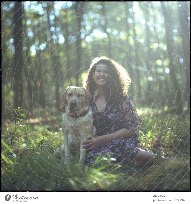 analoges Mittelformatbild: Junger, blonder Labrador im Wald mit einer großen, dunkelhaarigen Frau mit wilden Locken, die in die Kamera lächelt Freude schön