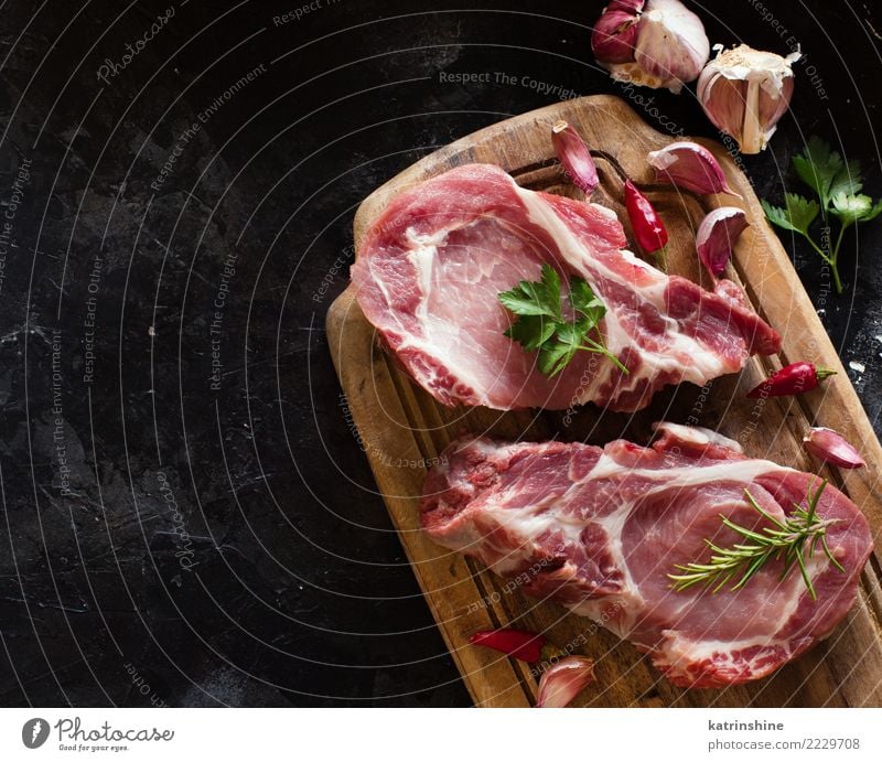 Rohe Schweinefleischsteaks nannten capicola mit Gemüse und Kräutern Fleisch Kräuter & Gewürze Ernährung Abendessen frisch oben grün rot Capicolla Holzplatte