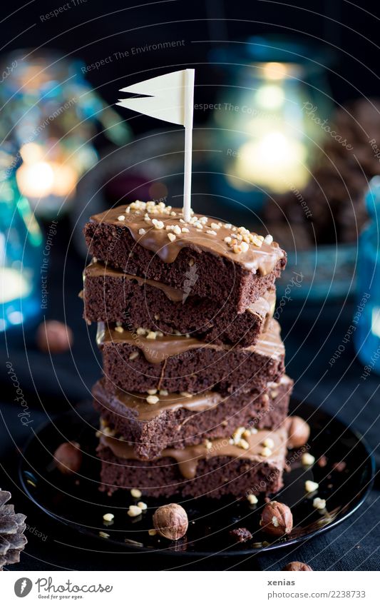 aufgetürmte Schokoküchlein mit Haselnuss und Fähnchen auf schwarzem Teller und blauen Lichtern im Hintergrund Kuchen Schokolade Brownie Schokoladenkuchen